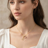 A close-up of a woman wearing a gold letter pendant necklace with a pink gemstone charm.