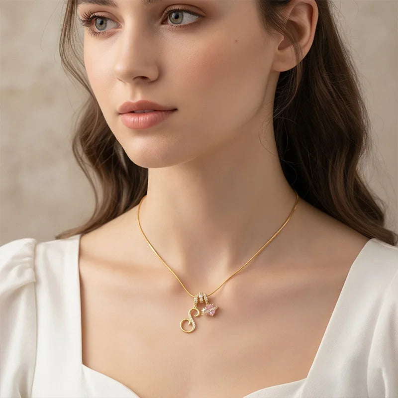A close-up of a woman wearing a gold letter pendant necklace with a pink gemstone charm.