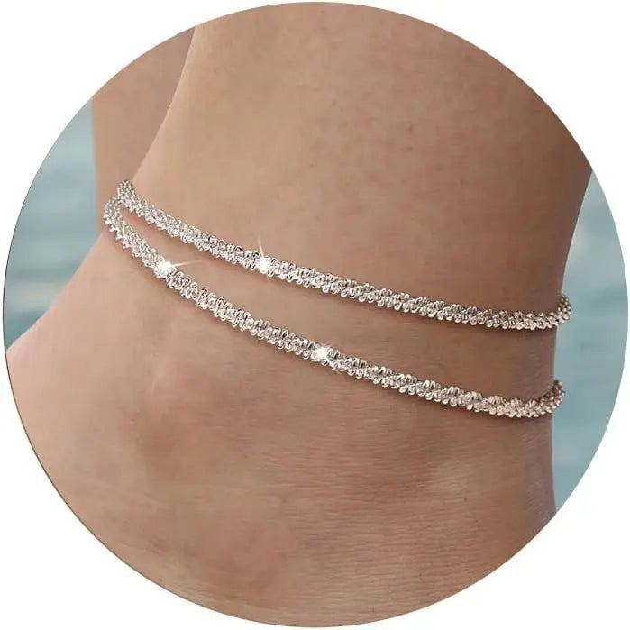 Gold plated glitter layered anklets worn on a person's ankle.
