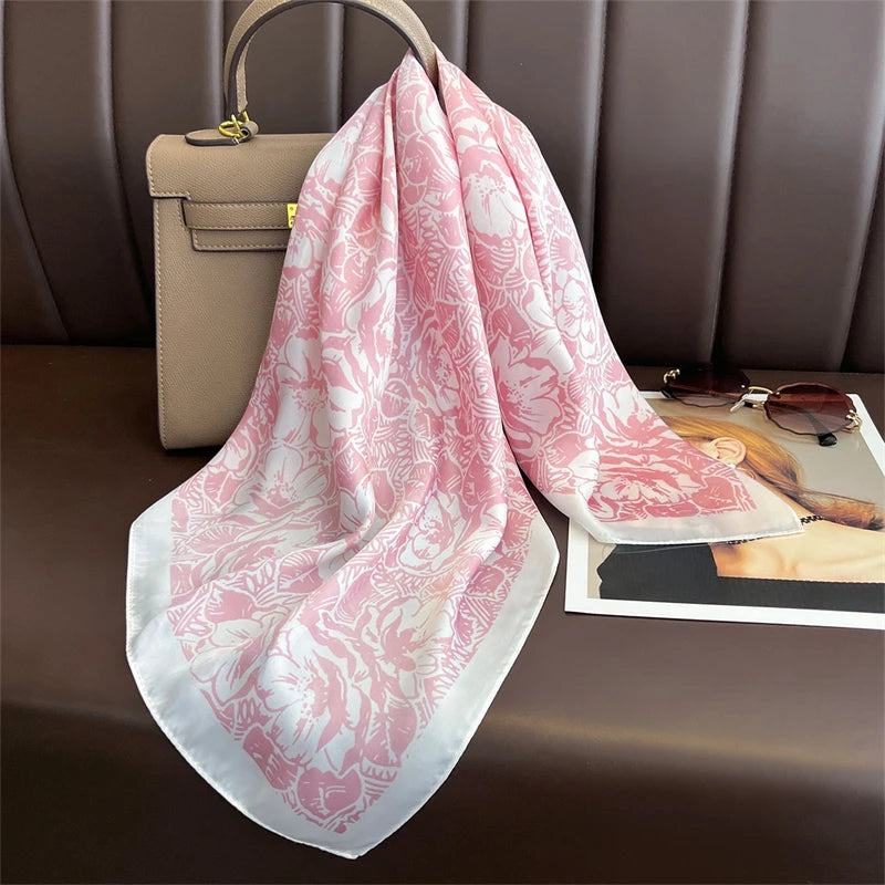 A pink floral silk scarf draped over a brown leather handbag on a dark surface.