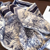 A close-up of a floral print silk scarf featuring intricate black and white botanical designs folded on a brown surface.