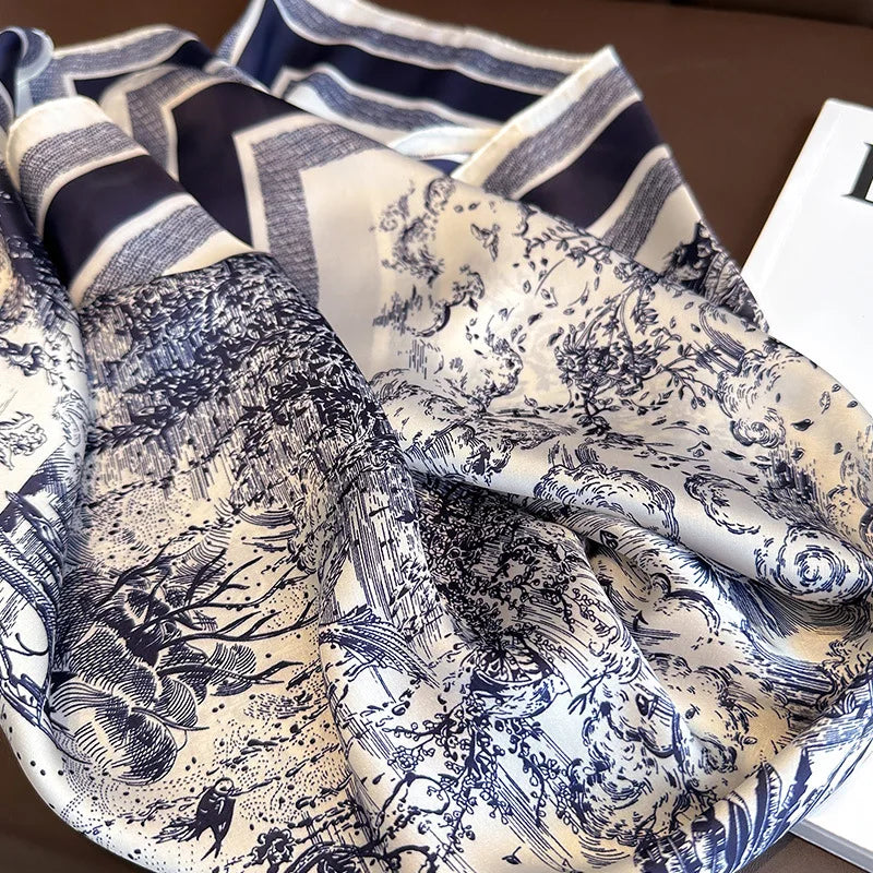 A close-up of a floral print silk scarf featuring intricate black and white botanical designs folded on a brown surface.
