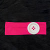 Pink stretch hairband with a white circular dot accent on a black fur background