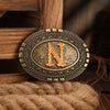 A vintage western belt buckle with an ornate gold letter N design resting on a wooden surface.