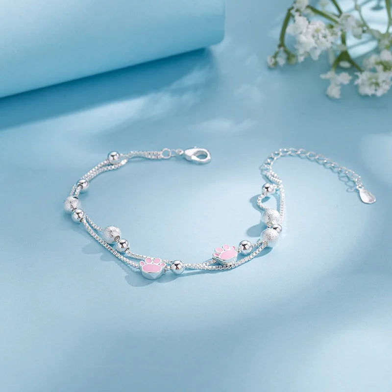 Sterling silver double heart charm bracelet displayed on a light blue background with white flowers in the blurred background