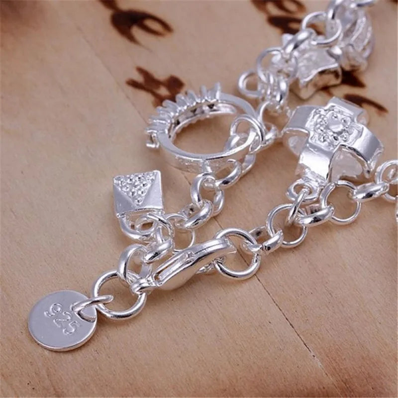 A silver geometric charm bracelet featuring various charms and links displayed on a wooden surface.