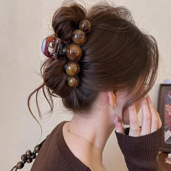 A woman's dark brown hair is styled in an elegant updo with a retro gradient beaded hair claw clip featuring amber and tortoi