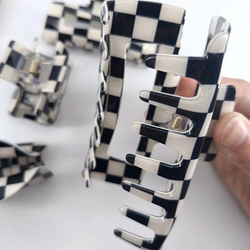 A hand holds a black and white checkered rectangle hair claw clip against a white background.
