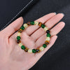 A bracelet made of various colored Tiger Eye crystals, including green, brown, and yellow-gold stones, is held in a hand.