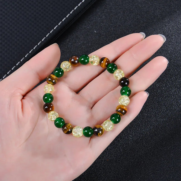 A bracelet made of various colored Tiger Eye crystals, including green, brown, and yellow-gold stones, is held in a hand.