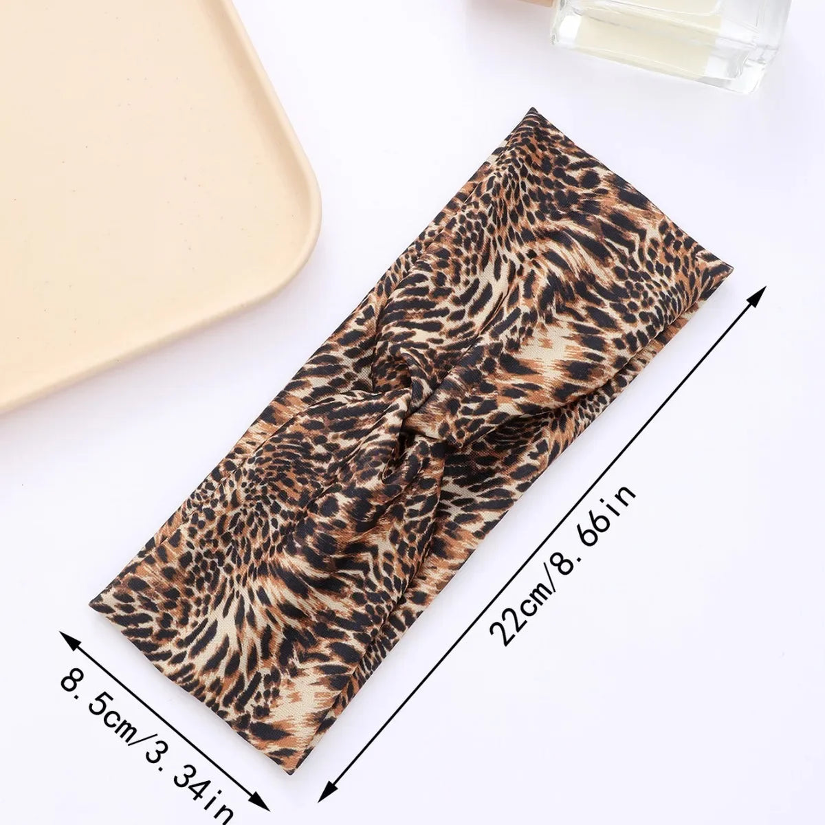 A close-up of a leopard print fabric headband tied in a bow, shown with size measurements.