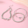 A set of three silver heart charm bracelets with delicate chains and crystals displayed on a pink background.