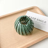 A green horsetail hair clip is displayed on a wooden tray next to a card.