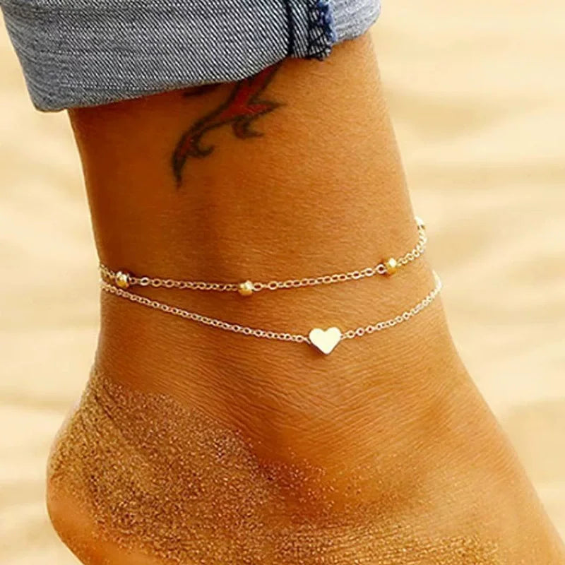 Gros plan d'un bracelet de cheville à perles d'or porté sur la cheville d'une femme, contre une peau hâlée.
