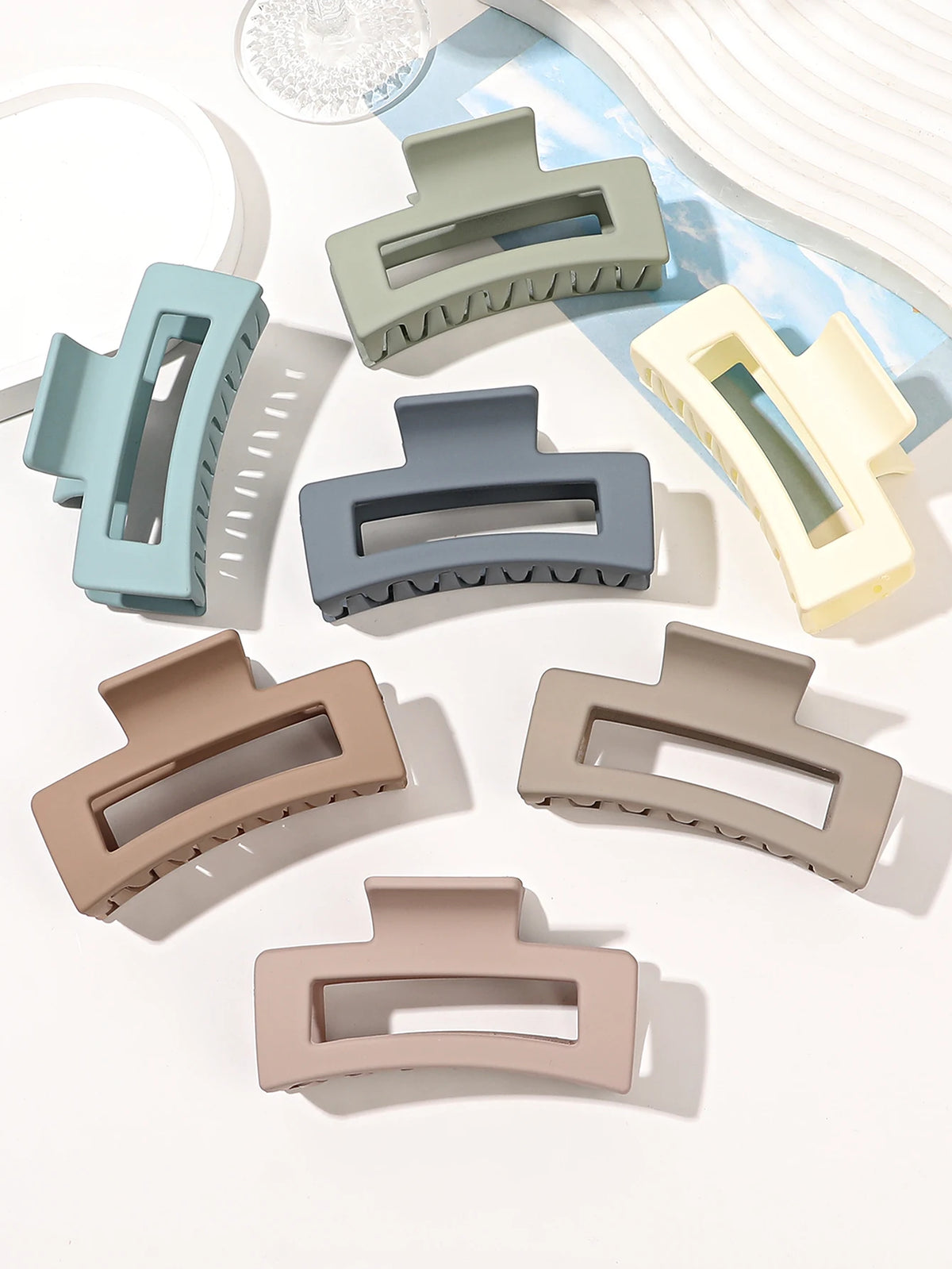 A set of seven square hair claw clips in various muted pastel and neutral colors displayed on a white background.