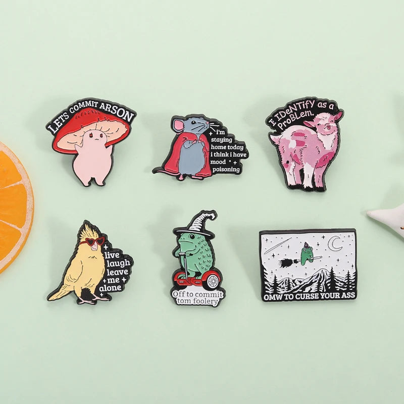 A collection of enamel pins featuring whimsical characters and humorous phrases.