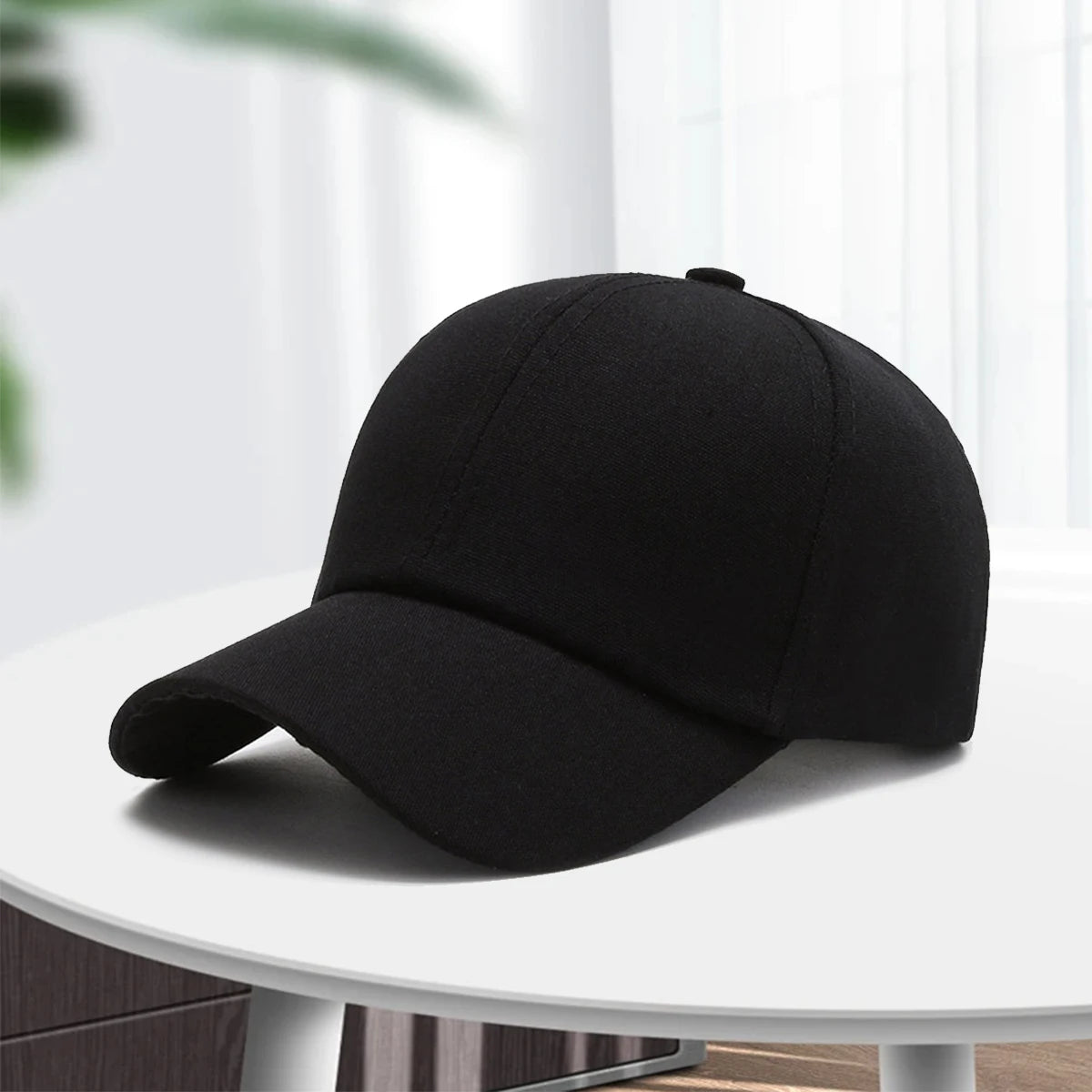 A black unisex cotton curved visor hat is displayed on a white table.