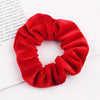 A close-up of a red velvet scrunchie, a soft elastic hair tie for women.