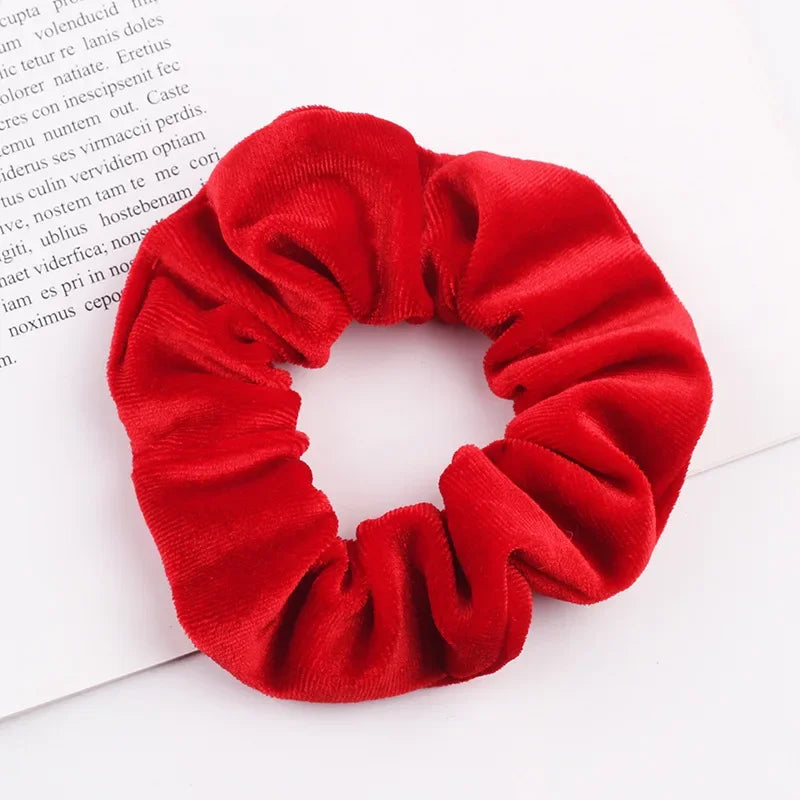 A close-up of a red velvet scrunchie, a soft elastic hair tie for women.