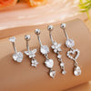 A set of five silver-toned stainless steel dangled belly button rings with floral and heart charms displayed on a beige surfa