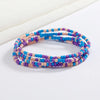 Una pila de pulseras de cuentas coloridas con tonos azules, morados y rosas sobre un fondo blanco.
