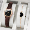 A brown leather watch and a gold heart pendant are displayed in a white box.