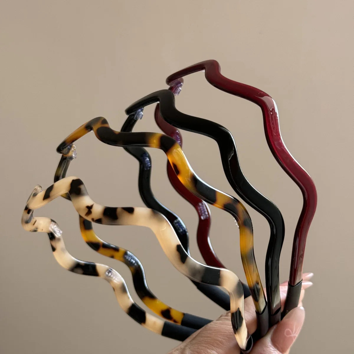 Una mano sostiene un set de aros para el pelo de acetato ondulado estilo tortuga con patrones oscuros y ámbar.