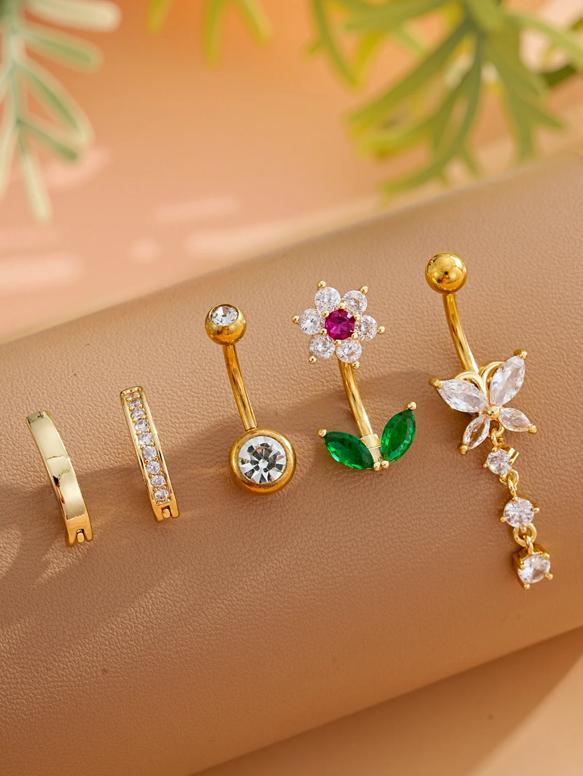 A set of five gold stainless steel dangled belly button rings featuring various gemstone and floral designs.