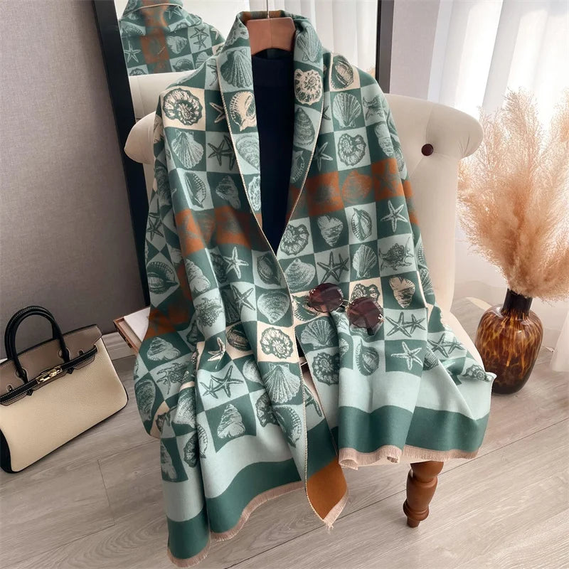 A draped scarf wrap featuring a plaid pattern of green and beige leaves and geometric shapes, displayed on a white chair.