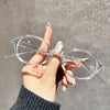 A hand holds a pair of clear round anti-blue light computer glasses against a gray background.