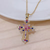 A dainty gold cross charm necklace featuring colorful gemstones including pink, blue, and purple stones.