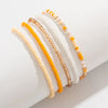 A set of five multi-layered beaded anklets in shades of yellow, white, and gold.