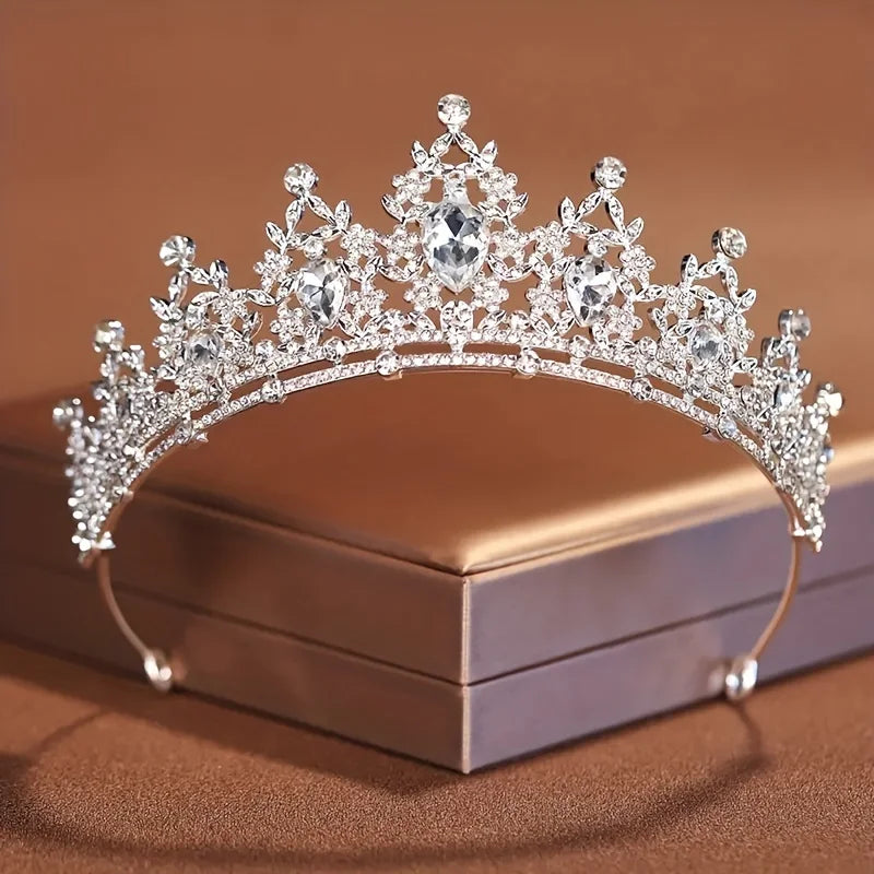 Diadema de cristal plateado brillante con intrincados diseños barrocos sobre una caja marrón.