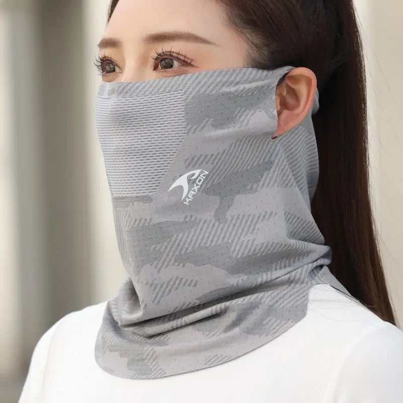 A woman wearing a gray camouflage face and neck gaiter with a white logo, against a light background.