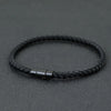A black braided thread bracelet with a silver clasp is displayed on a dark surface.
