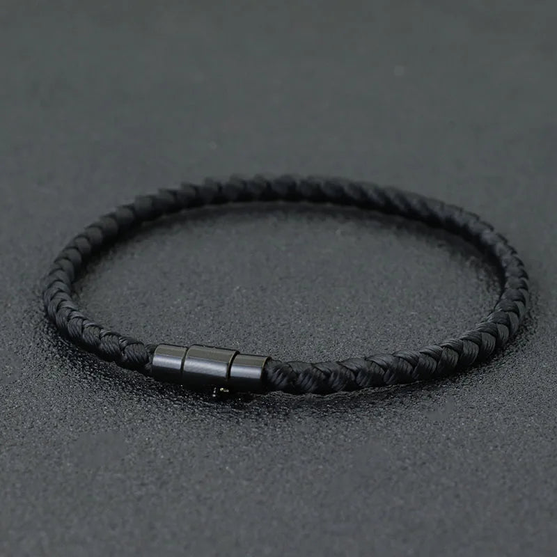 A black braided thread bracelet with a silver clasp is displayed on a dark surface.
