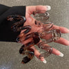 A pair of high-gloss amber hair clips shaped like spirals are held in a person's hand against a dark suit jacket.