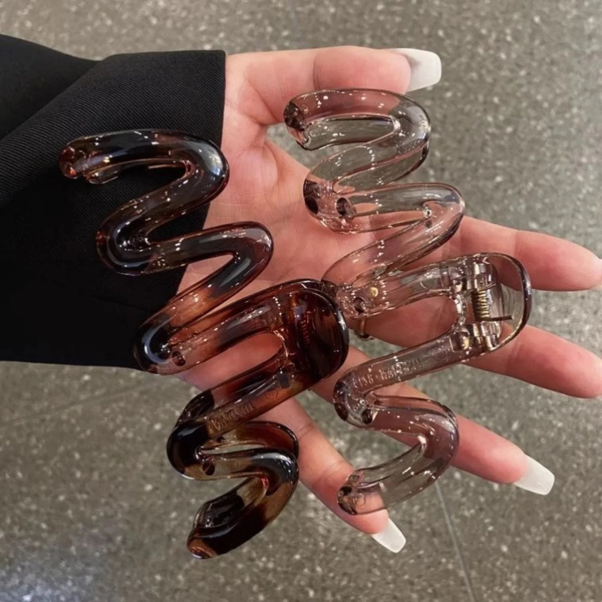 A pair of high-gloss amber hair clips shaped like spirals are held in a person's hand against a dark suit jacket.