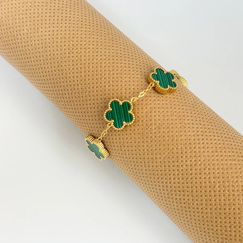 Gold plated stainless steel double-sided petal bracelet with green enamel petals on a brown textured background