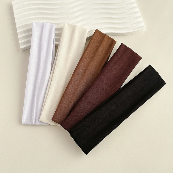 A collection of five solid colored fabric headbands in white, cream, brown, maroon, and black laid out on a light surface.