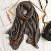 Dunkel gemusterter Seid-Pashmina-Schal auf weißer Fläche neben einem goldenen Rahmen und einer schwarzen Ledertasche.