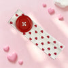 A white headband with red hearts and a large red polka dot button, lying on pink surface.
