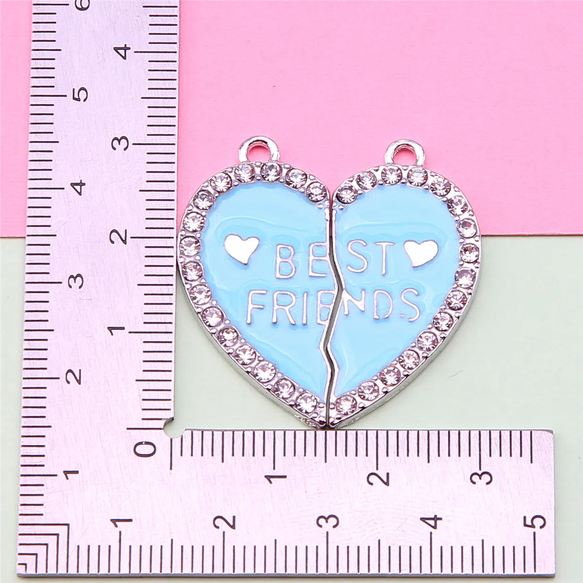 Colgante de amistad en forma de corazón con esmalte azul y detalles plateados, medido contra una regla.