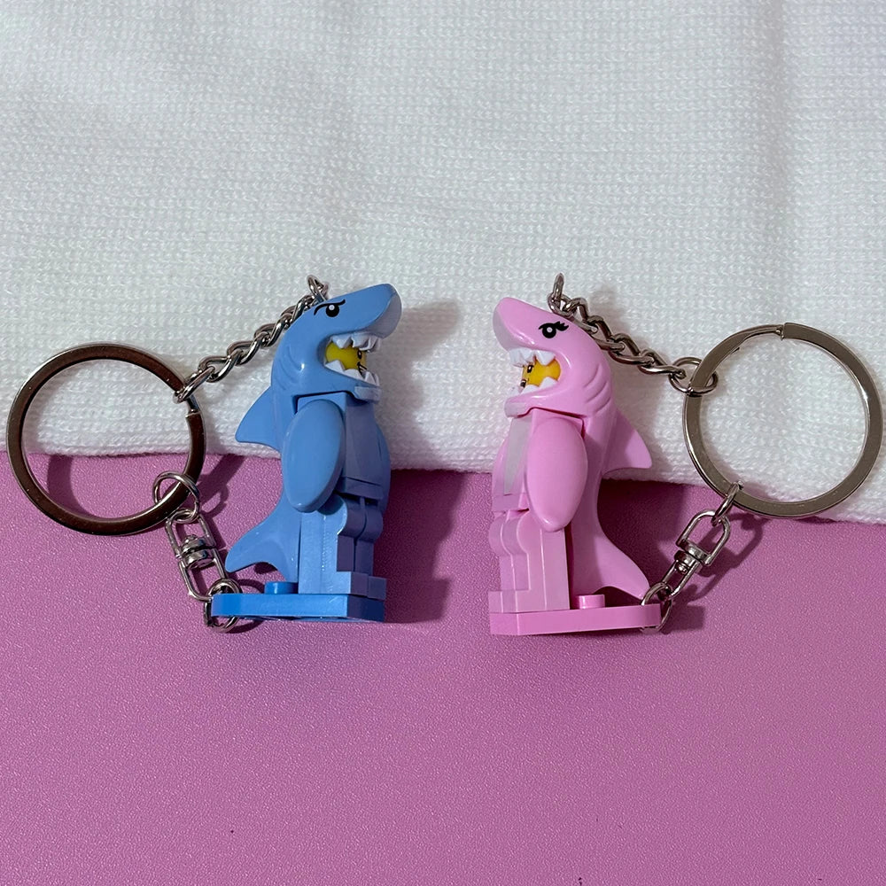 A pair of heart-shaped building block keychains featuring blue and pink shark figures attached to silver split rings.