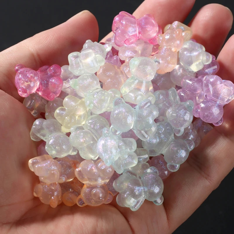 A handful of luminous glow-in-the-dark acrylic beads in shades of pink, purple, and pale green are held in a hand.