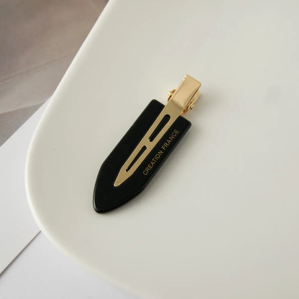 Une pince à cheveux noire avec des accents dorés et le texte Creation France sur une surface blanche.