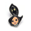 Broche émail noire avec un visage fantomatique stylisé, des yeux jaunes et une peau claire.