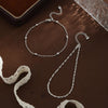 Silver gold-plated twisted ankle bracelets displayed on a dark brown surface.
