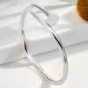 Silver stainless steel ring with a four-leaf clover charm resting on a white surface.