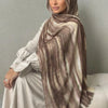 Una mujer vistiendo un elegante pañuelo de hijab a rayas marrón y beige sobre una ropa de color claro.